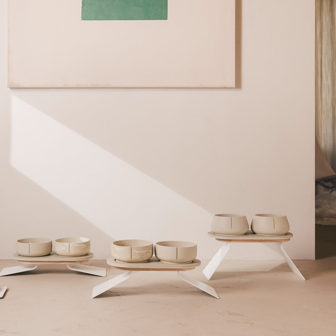 Three PINO raised feeders set at different heights, sandstone bowls on wooden trays with white steel legs