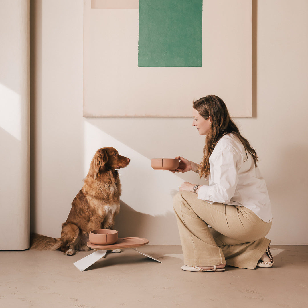 Vrouw geeft haar hond een PINO voerbak naast een verhoogd PINO Plateau